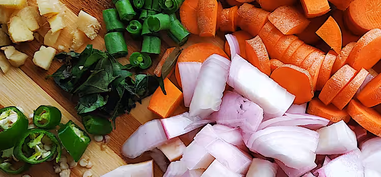 Chopped fresh onions, carrots, chillies and ginger on a board.