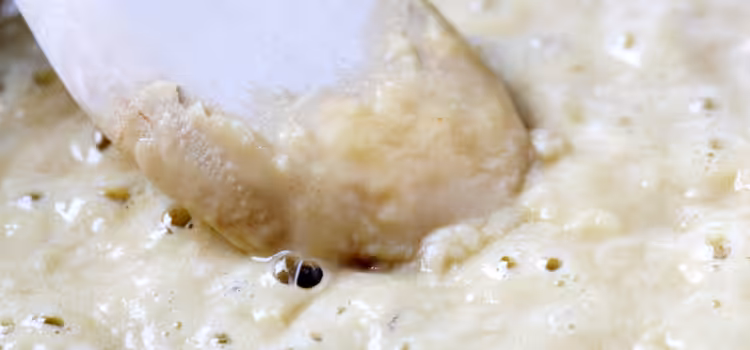 Closeup of butter and flour bubbling in a pan around the tip of a wooden spoon.