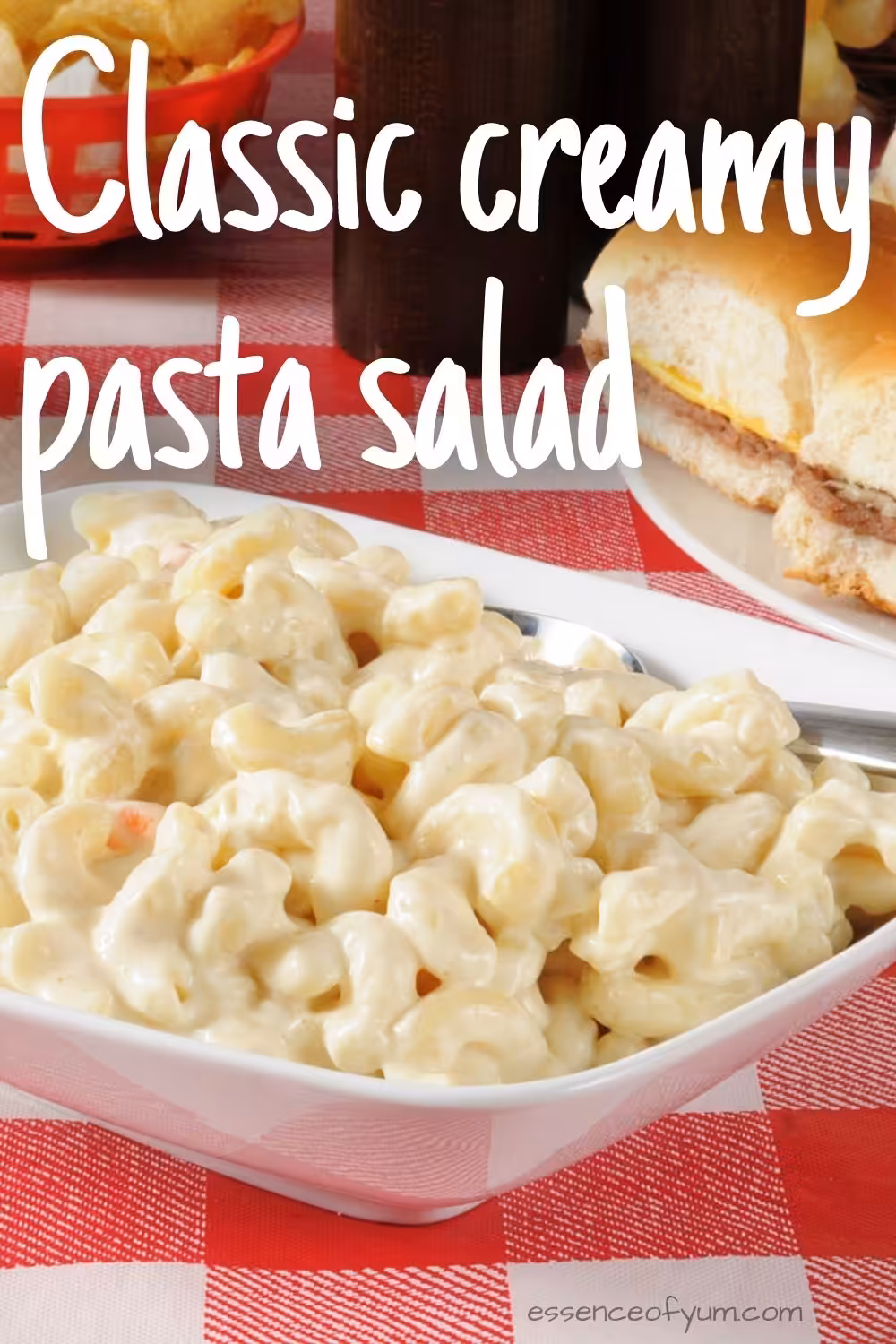 Closeup of a white bowl full of creamy macaroni salad on a bright red and white tablecloth with the text classic creamy pasta salad.