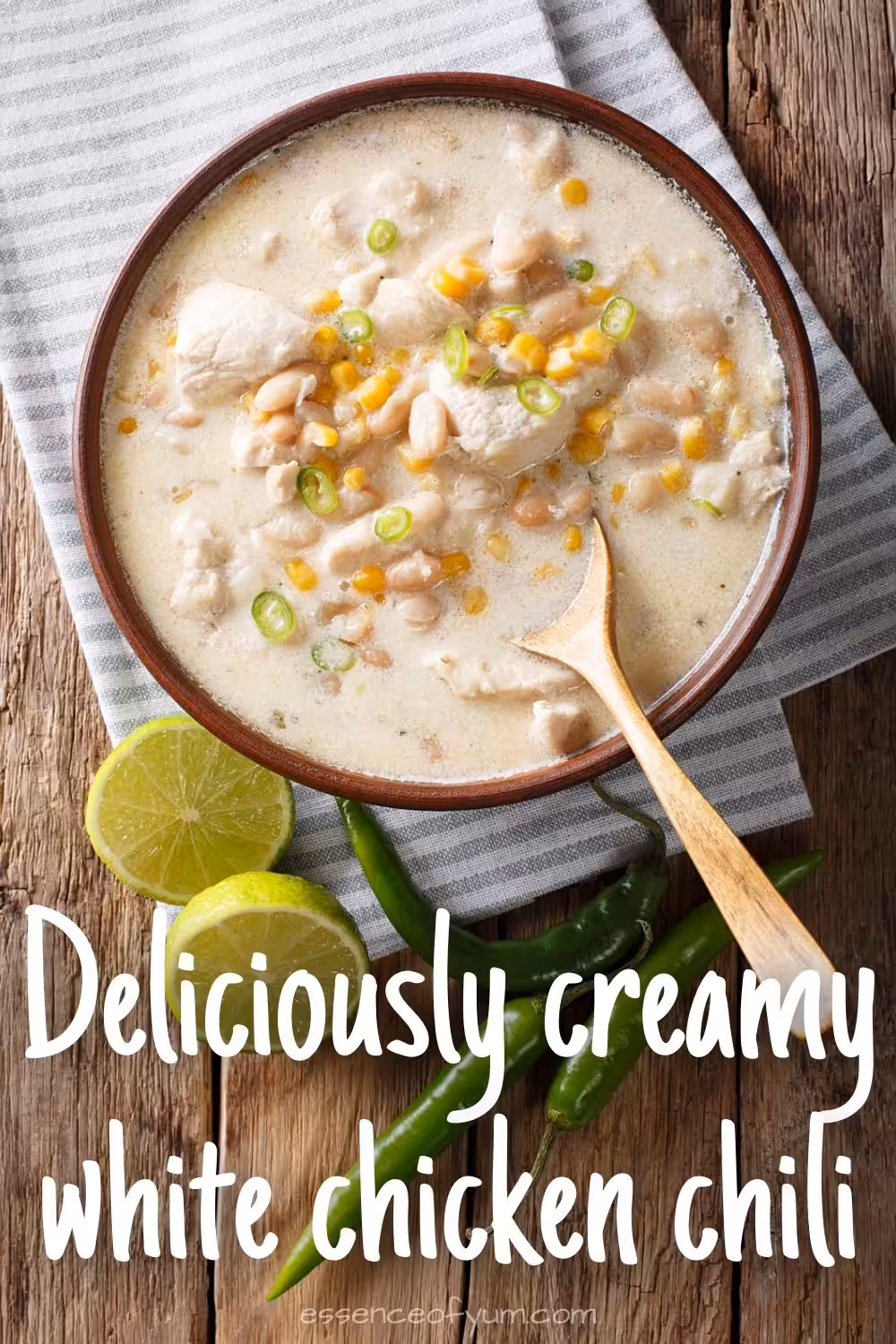 A bowl of creamy white bean chicken chili with a wooden spoon and vibrant green chilis and limes next to it, plus the text deliciously creamy white chicken chili.
