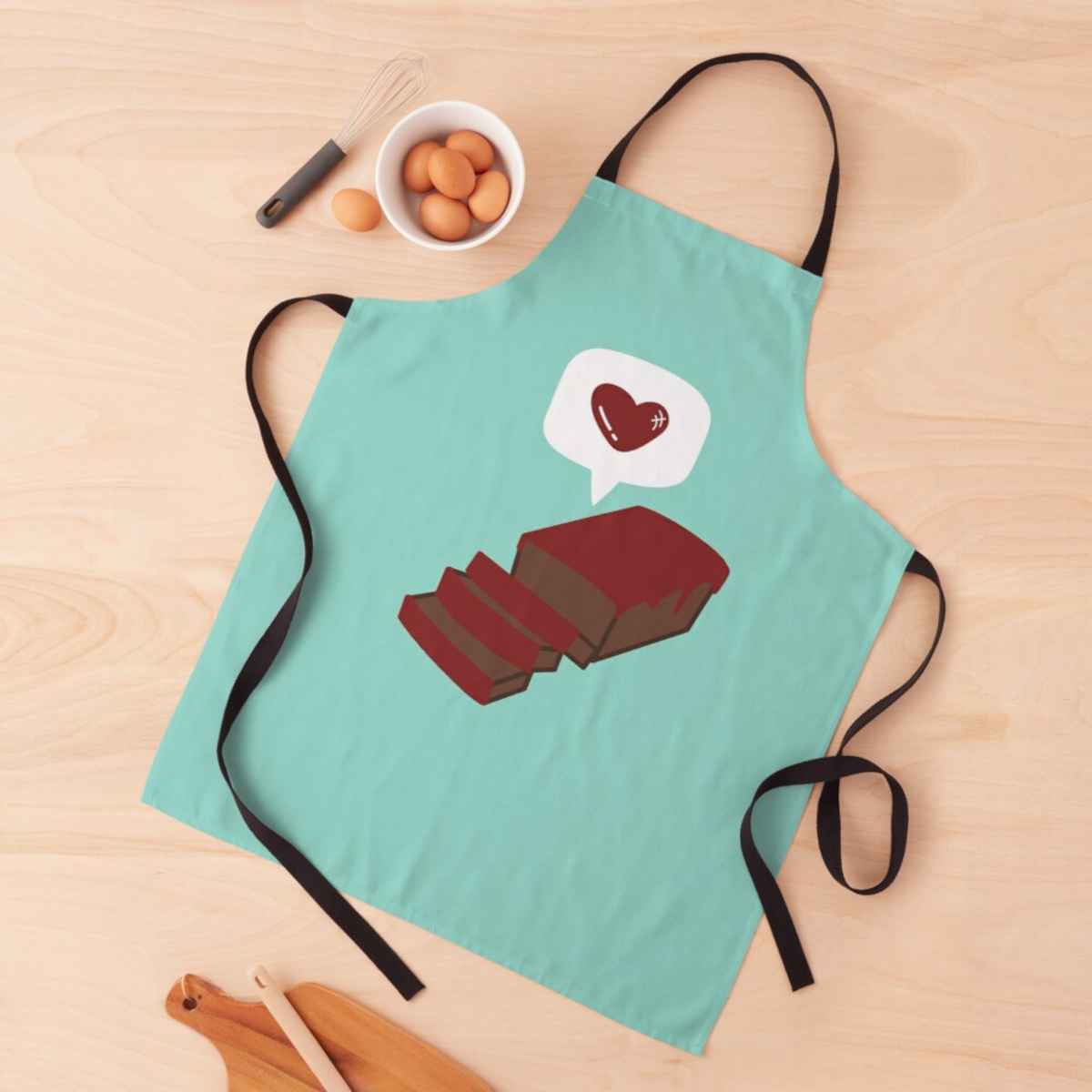 A green apron on a wooden surface with a drawing of a meatloaf and a heart above it.