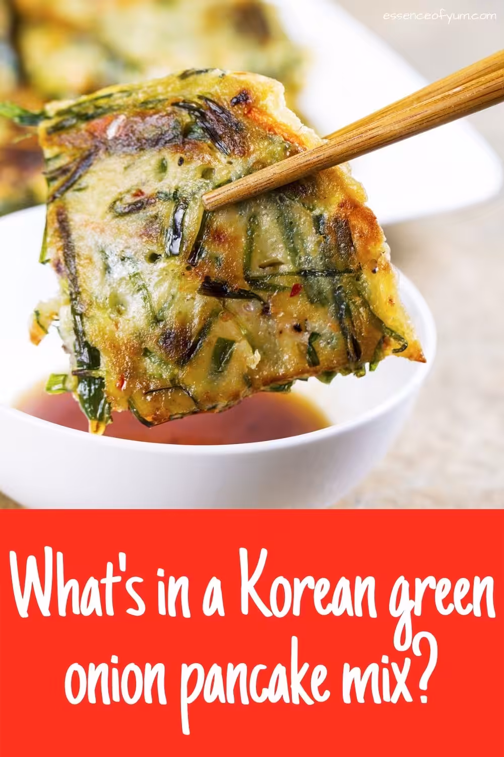 Closeup of a wedge of scallion pancake held in chopsticks over a white bowl of dipping sauce with the text what's in a Korean green onion pancake mix.
