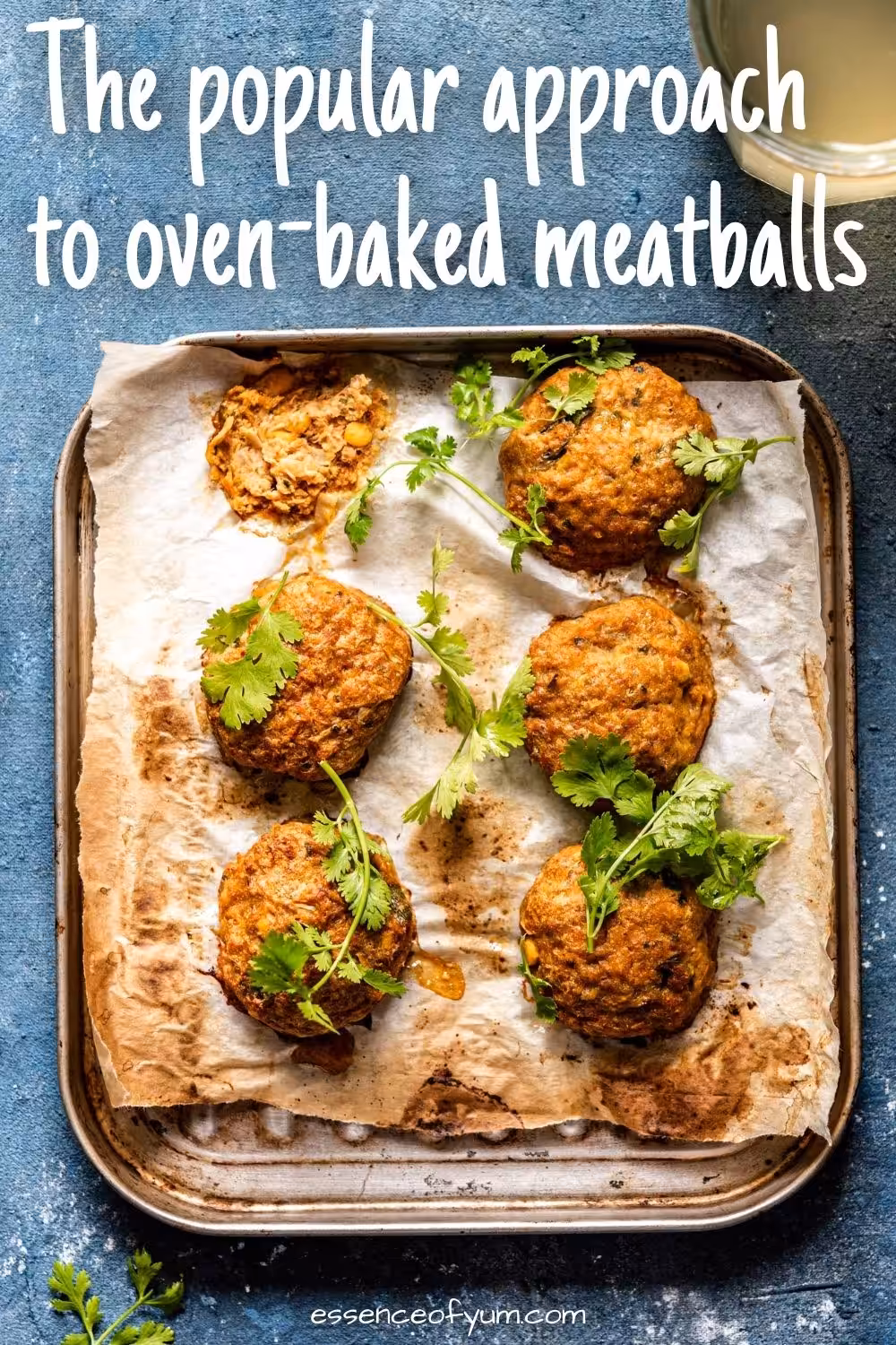 Six browned meatballs on parchment paper on a baking tray garnished with cilantro and the text the popular approach to oven baked meatballs.