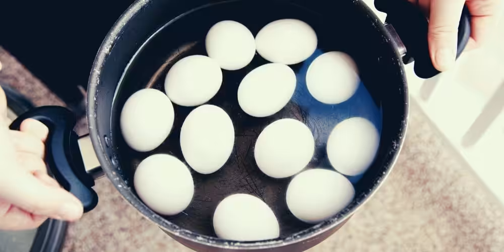 Closeup of a dozen eggs in water in a large pot.