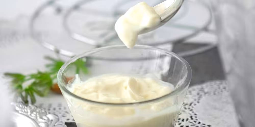 Closeup of a small glass bowl with mayonnaise in it and a dollop on a spoon above it.