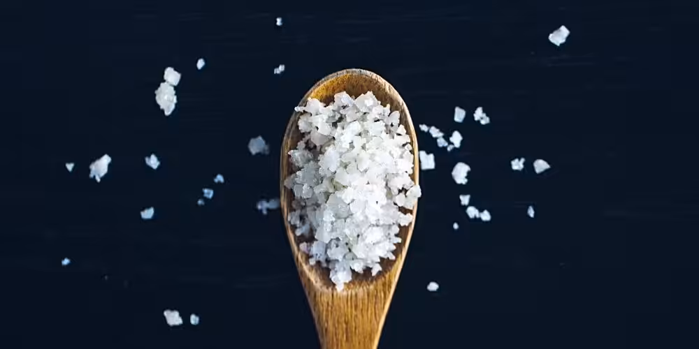 Closeup of a wooden spoon full of large salt crystals.