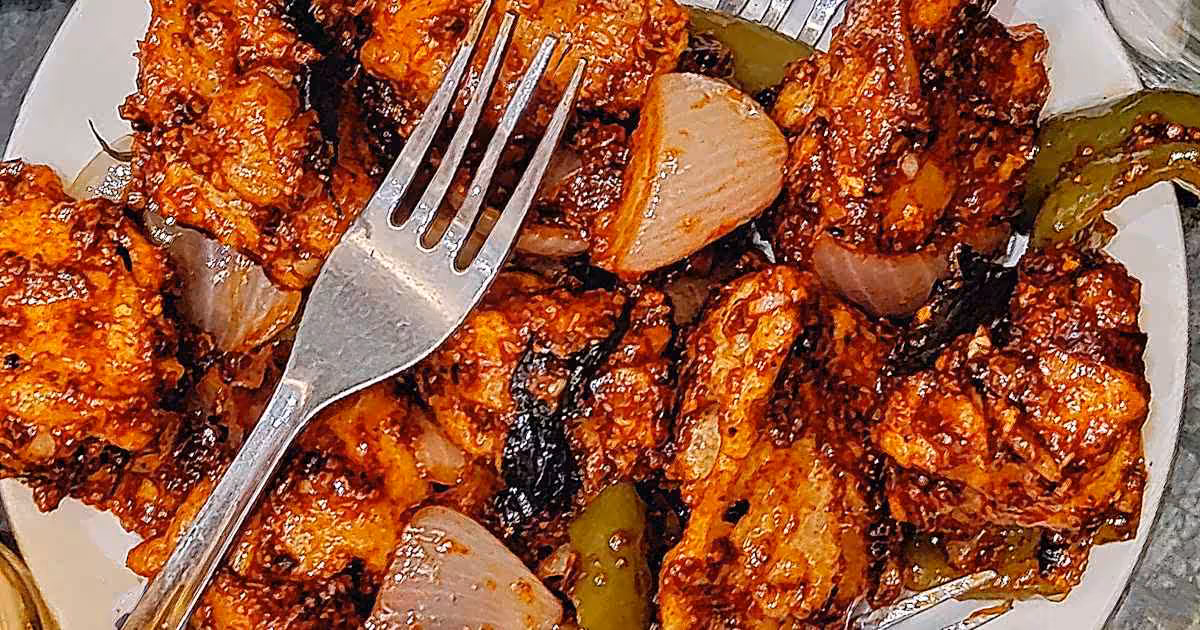 Closeup of a white plate loaded with sticky Chicken 65 in gravy.