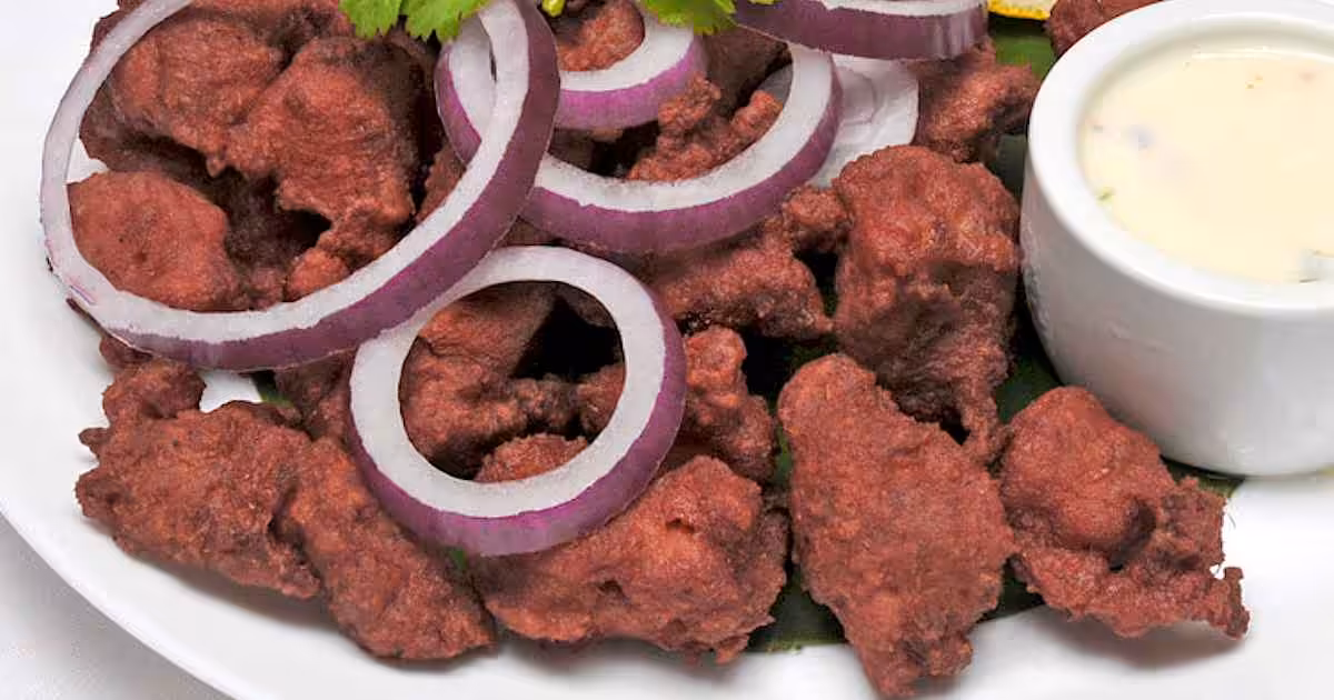 Closeup of a white plate full of bright red dry Chicken 65, garnished with onion slices and cilantro.