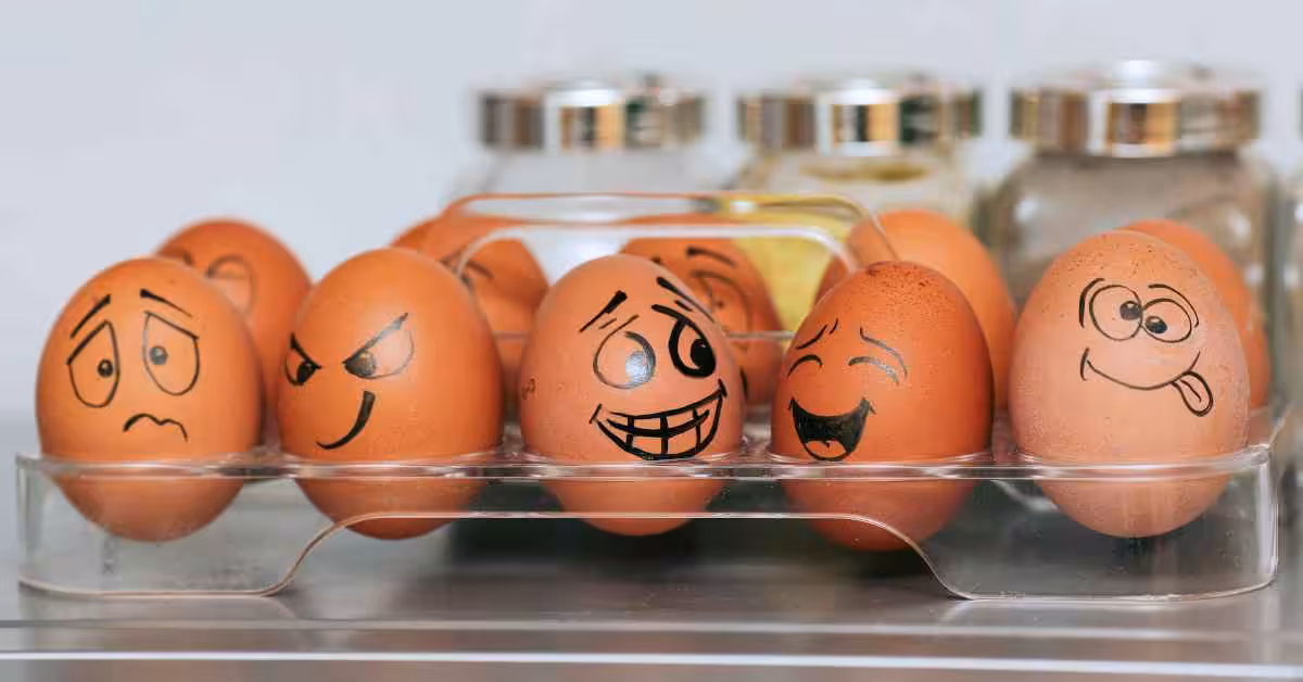 Closeup of ten eggs in an egg tray each with funny faces drawn on them.