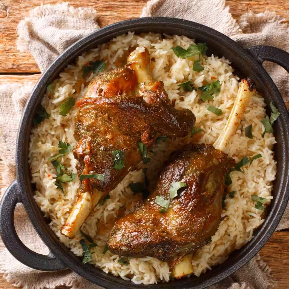A casserole dish full of basmati rice with two golden brown Yemeni haneeth lamb shanks on top.