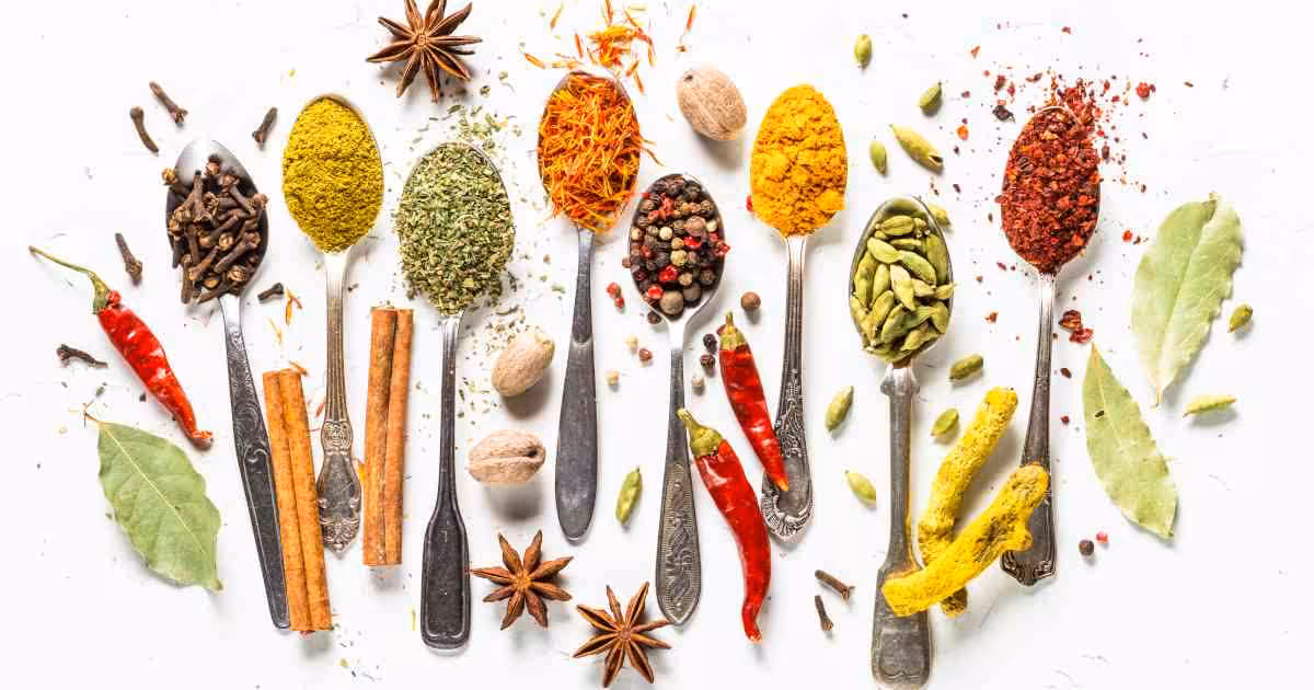 A collection of different spices on spoons and the white surface around them.